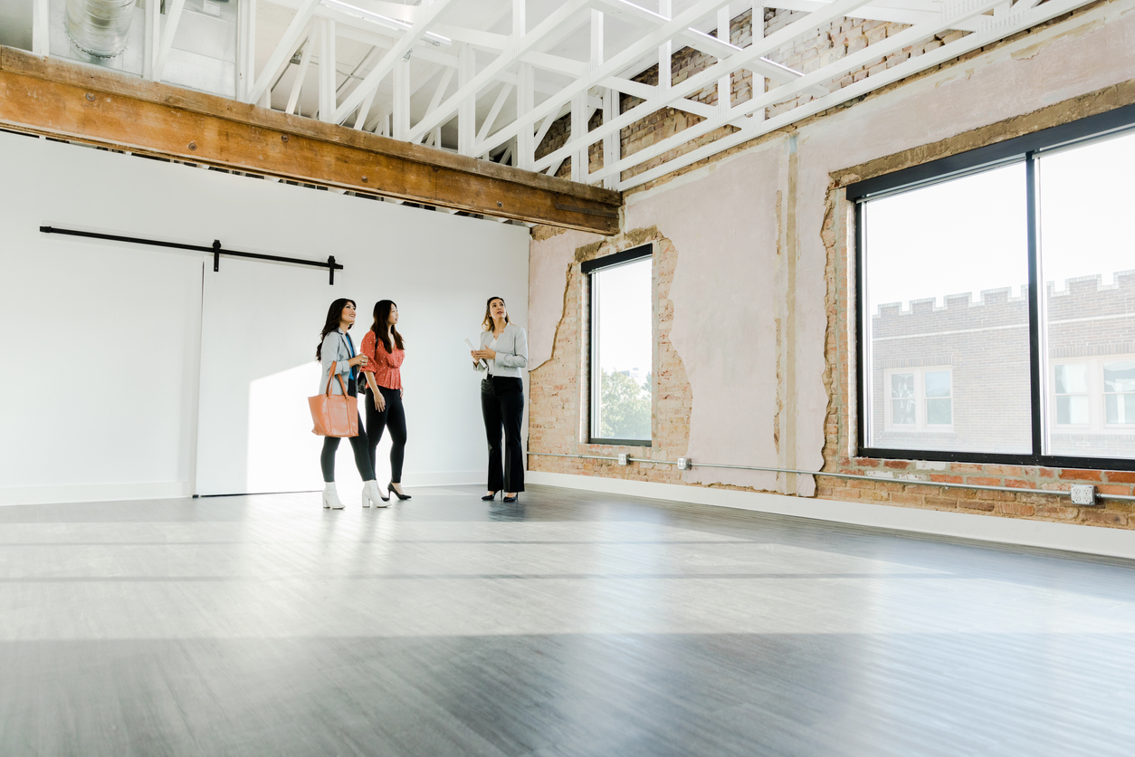 The mid adult female real estate agent shows two businesswomen an open loft in the city used for office space.