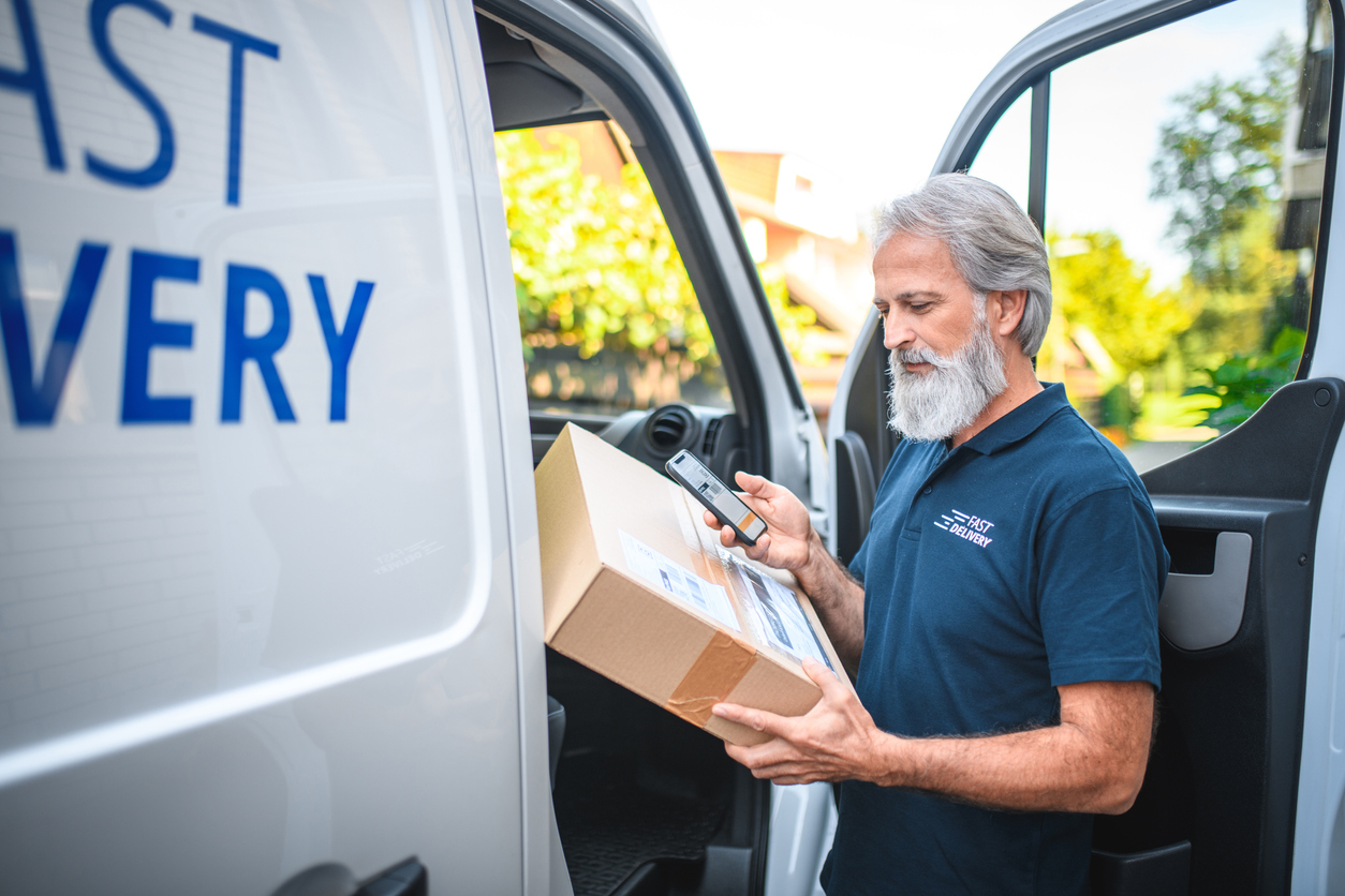 Mature delivery man with beard delivering the package to client, scanning the label.