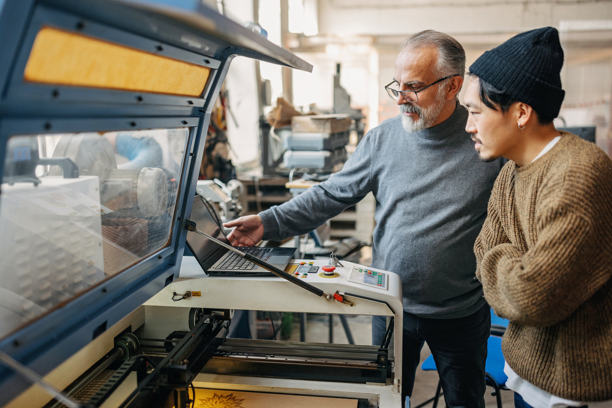 Mid adult man teaching young asian student how to operate laser cut machine