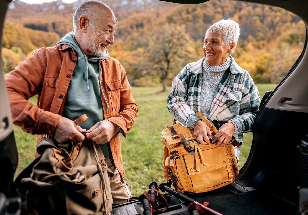 Senior couple getting ready for hiking, taking stuff from a car trunk
